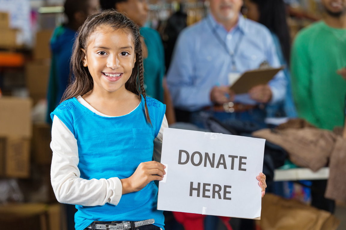 Little girl holding ""donate here"" sign at food/clothing bank
